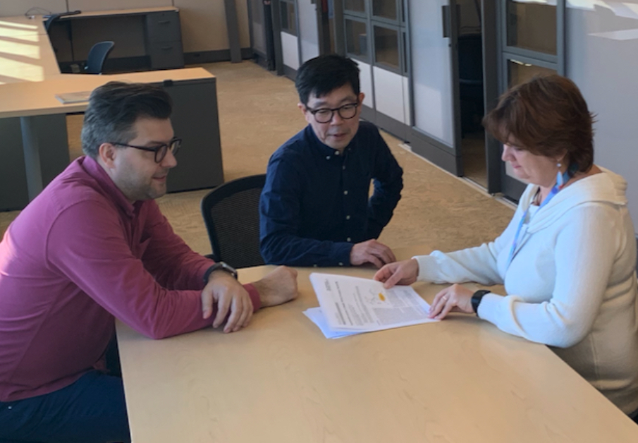 Three scientists around a table discuss plans for an EIC.