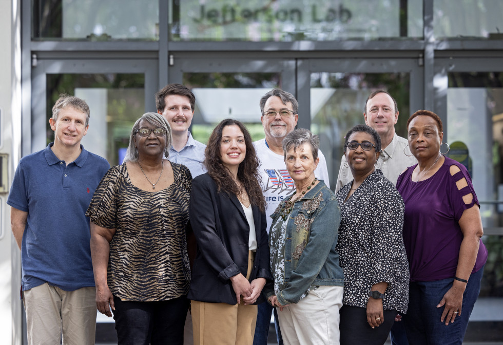 Nine members from the Jefferson Lab procurement team stand together and pose for a professional picture.