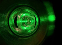 A close-up view of a green laser beam inside a reflective cylindrical chamber, which is the Compton polarimeter’s laser system