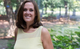 Clair Papas head & shoulders portrait in yellow shirt, trees in background