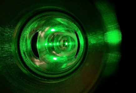 A close-up view of a green laser beam inside a reflective cylindrical chamber, which is the Compton polarimeter’s laser system