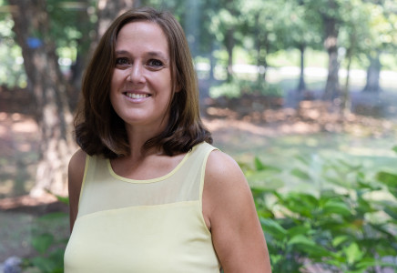 Clair Papas head & shoulders portrait in yellow shirt, trees in background